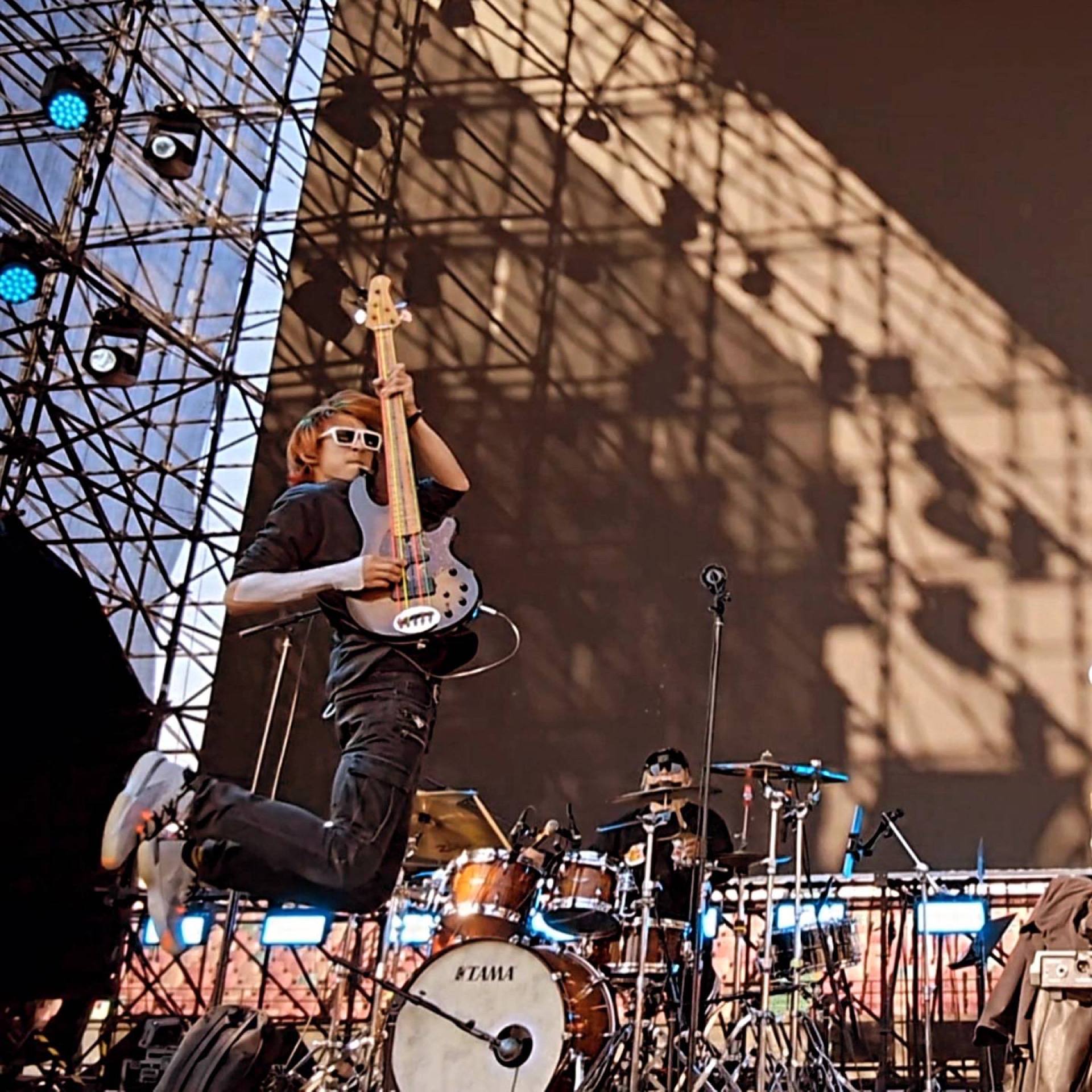 Sasha Wu mid-jump on a festival stage holding a bass